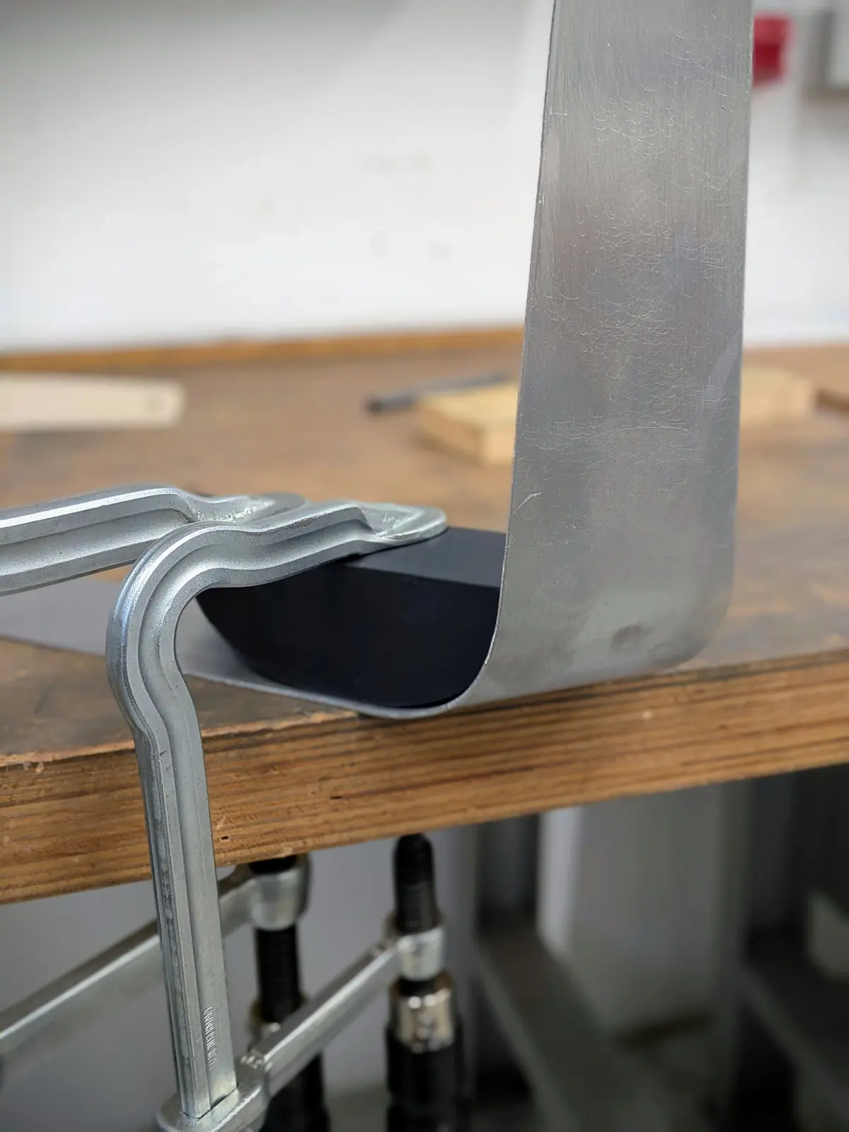A 2 mm part being bent over the edge of a workbench, clamped as a jig.