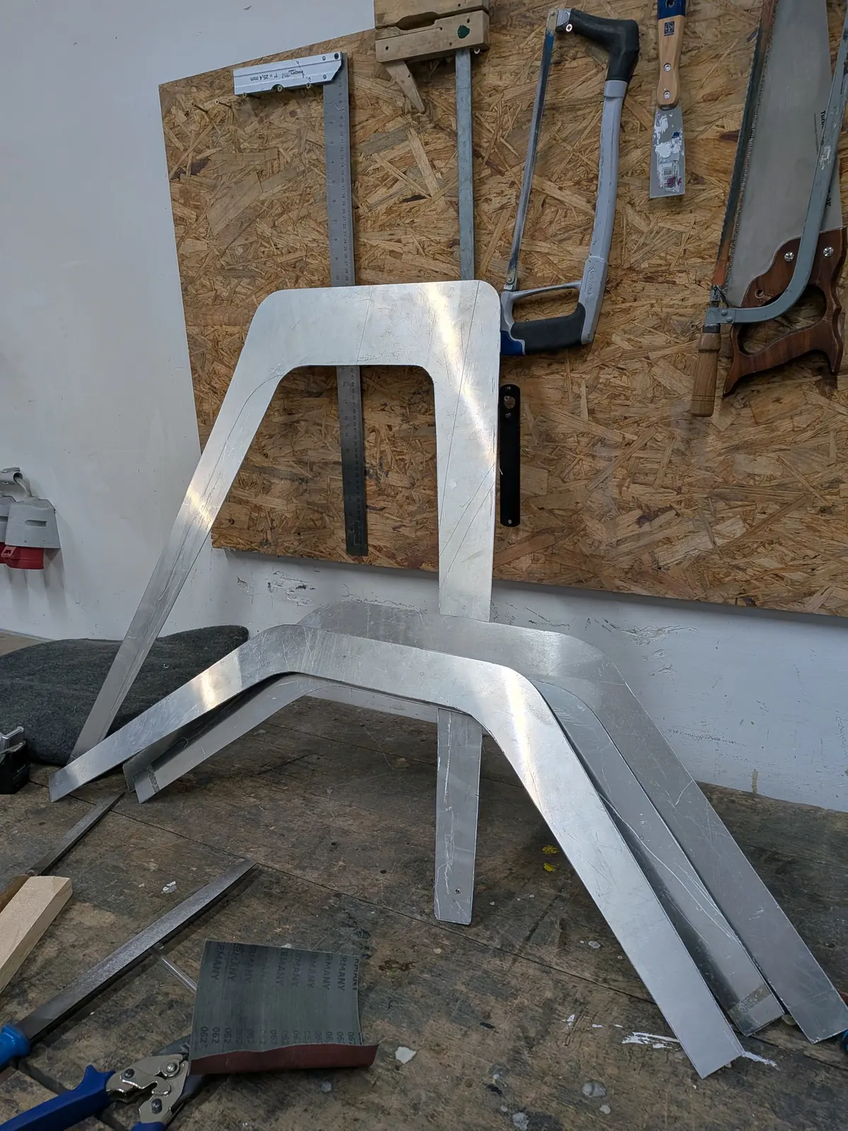 Hand-cut 2 mm aluminium parts leaning against a board, the leg profiles already bent.