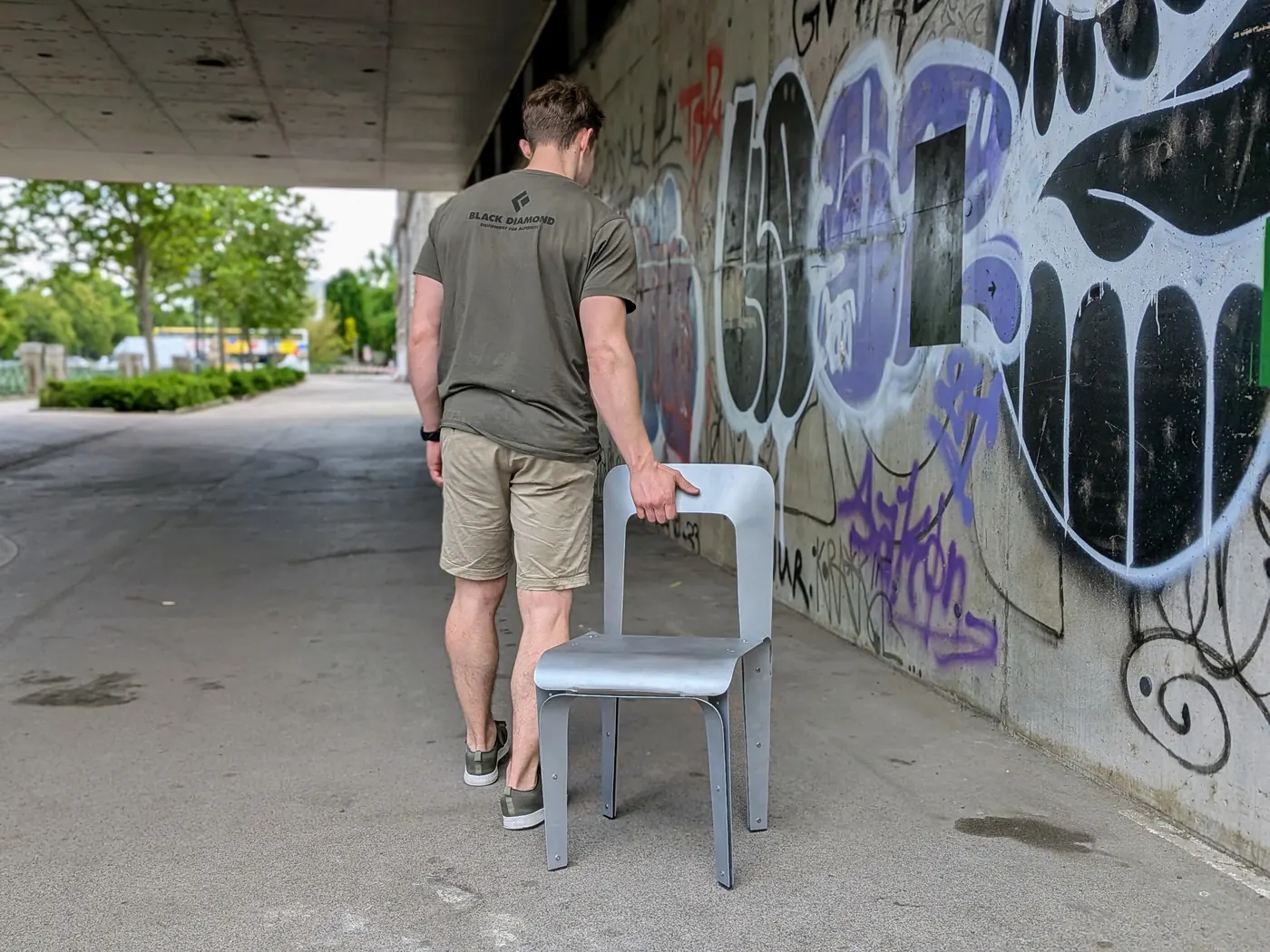 The 2 mm chair carried outdoors past a graffiti wall, held by one leg.