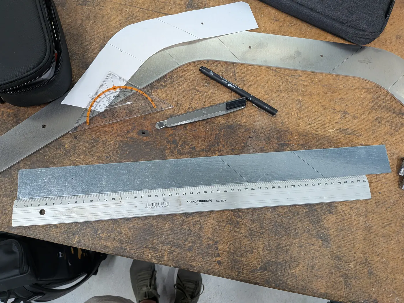A laser-cut 4 mm part on the bench with a steel rule, a protractor and the paper pattern laid over it.