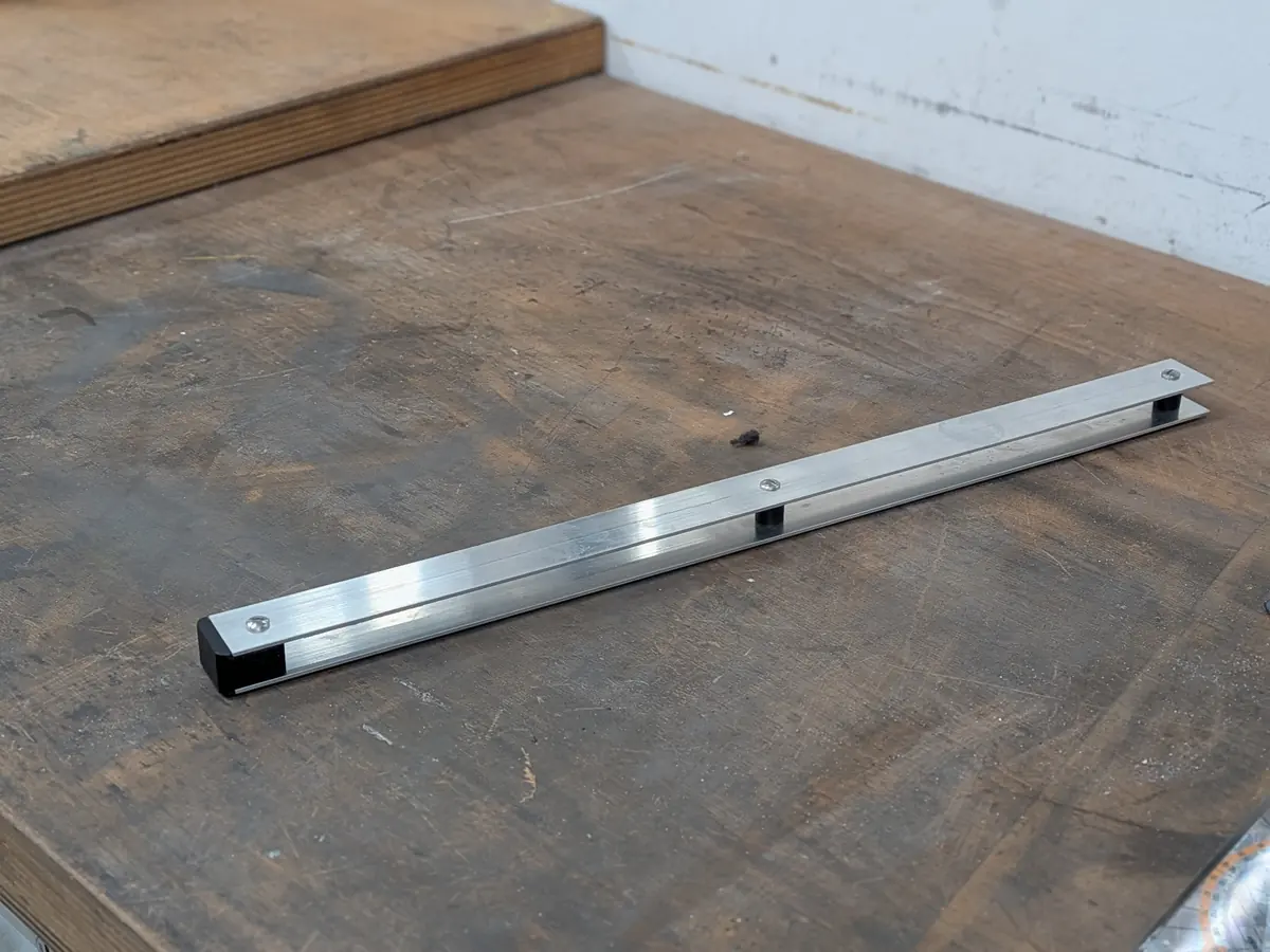 Two strips of aluminium joined with furniture screws through a spacer, on a workbench.
