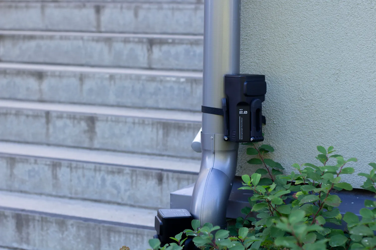 A unit strapped to a downpipe on a building, a second unit standing on the ground below.